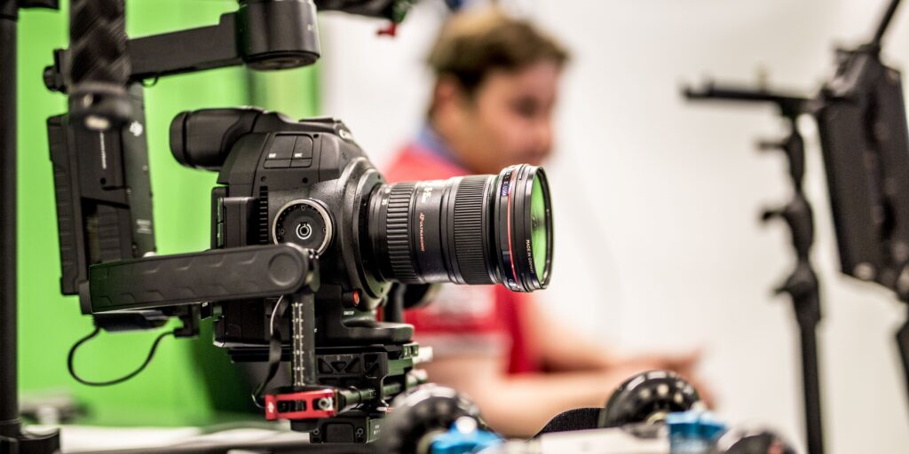 a video camera in the foreground with a greenscreen and person in the background